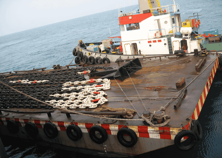Anchor chains being transported via tug and barge